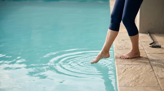 A senior person moving from land-based support into calm pool water, symbolizing pain-free movement